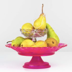 silver pear necklaces sat on a pile of pears on a pink cake stand