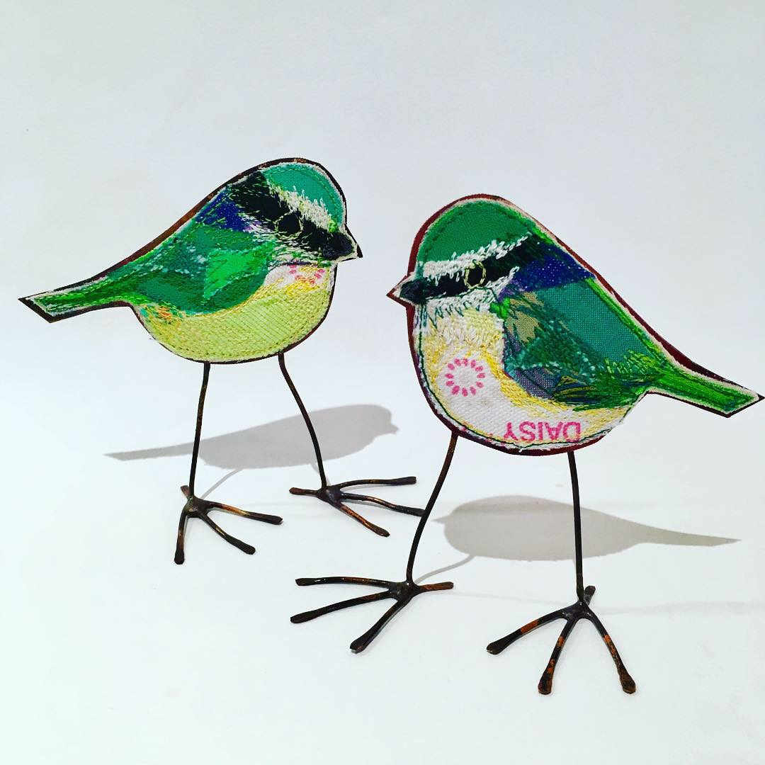 Two greeny blue tit embroidered birds with copper bodies.